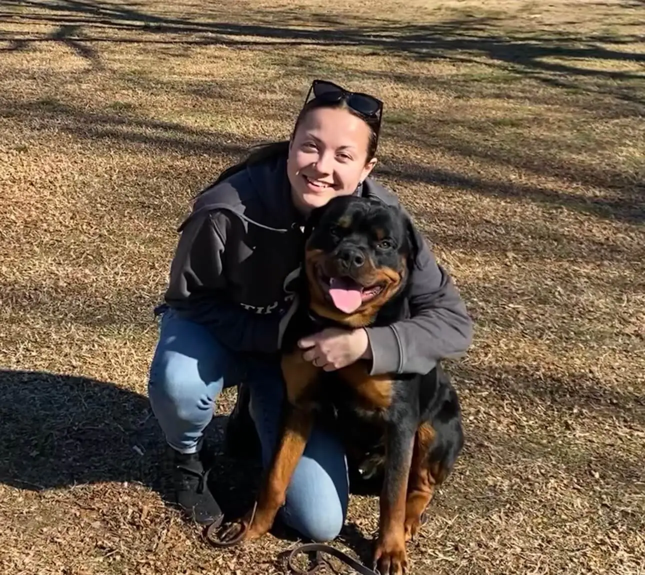 Tip Top K9 NW Arkansas trainer Alyssa calmly hugging a relaxed Rottweiler outdoors — proof that reactive and aggressive dogs can learn to settle